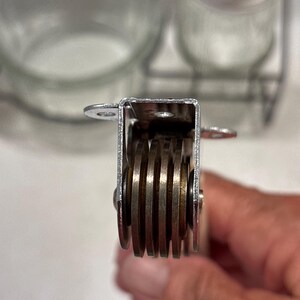 May include: A kitchen tool featuring a silver-colored metal frame with four parallel, circular cutting blades arranged vertically. The device includes small mounting tabs on the top sides, and the blades are held in place by a central metal pin.