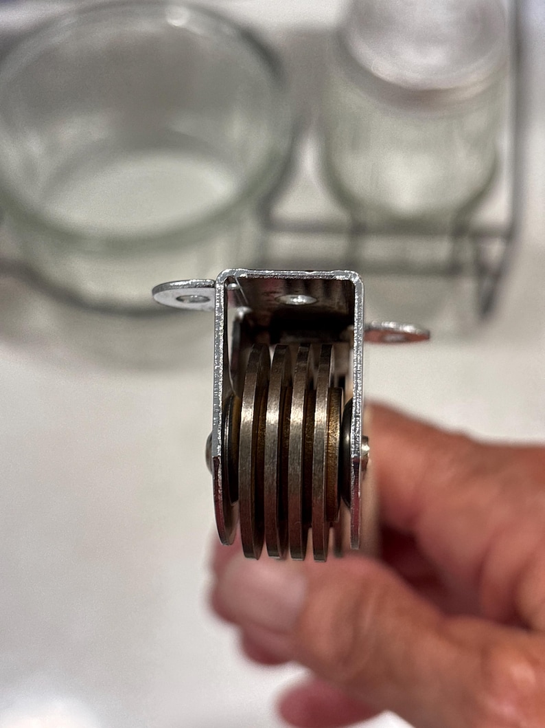 May include: A kitchen tool featuring a silver-colored metal frame with four parallel, circular cutting blades arranged vertically. The device includes small mounting tabs on the top sides, and the blades are held in place by a central metal pin.