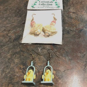 May include: Two pairs of resin earrings. The first pair features a yellow bunny with a pink dress and blue accents. The second pair features a yellow chick on a blue swing. The packaging reads "Cottontail Collection Resin Bunny Earrings".