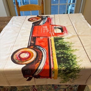 Peut inclure: Nappe rectangulaire avec un camion rouge vintage transportant un sapin de Noël. Le camion porte l'inscription "Magnolia" sur le côté. Le fond est un motif de grain de bois clair.