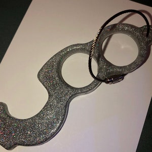 May include: Silver glitter door opener with a black string attached. The door opener has three loops for opening doors without touching surfaces.