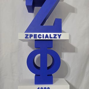 Puede incluir: Un expositor vertical con letras y símbolos azules apilados sobre estantes blancos. La estructura incluye el número 2, una paloma blanca, la letra Z, el texto ZPECIALZY, las letras griegas Phi y Beta, y el número 1920 en letras azules.