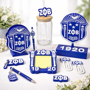 May include: A collection of blue and white ZOB-themed items, including a glass jar with a straw, pens, paper clips, a notepad holder, and decorative signs. The items feature the Greek letters ZOB and the year 1920.