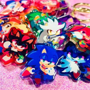 Op de afbeelding: Een verzameling kleurrijke sleutelhangers met cartoonfiguren, waaronder Sonic the Hedgehog, Shadow the Hedgehog en Silver the Hedgehog. De sleutelhangers zijn gemaakt van helder acryl met glitter ingebed in het plastic.