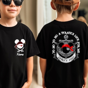 Puede incluir: Camiseta negra con un diseño de Mickey Mouse con temática pirata en la parte delantera, y un ancla de barco pirata con el texto "Yo Ho Ho A Pirate's Life For Me" en la parte trasera. El diseño incluye el texto "Disney 2026".