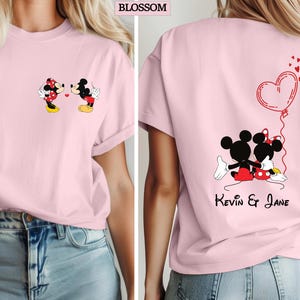 May include: A light pink t-shirt featuring Mickey and Minnie Mouse. The front of the shirt shows the characters kissing, while the back displays them embracing with a heart-shaped balloon and the names "Kevin & Jane". The word "BLOSSOM" is at the top.