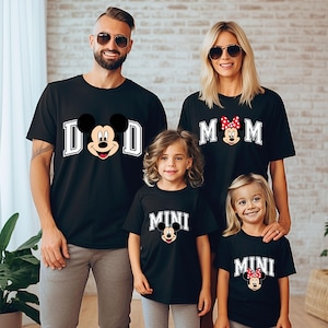 Puede incluir: Cuatro camisetas negras con diseños de Mickey y Minnie Mouse. Las camisetas dicen "DAD", "MOM" y "MINI". La camiseta "DAD" presenta a Mickey Mouse, la camiseta "MOM" presenta a Minnie Mouse y las camisetas "MINI" presentan a Mickey y Minnie Mouse.