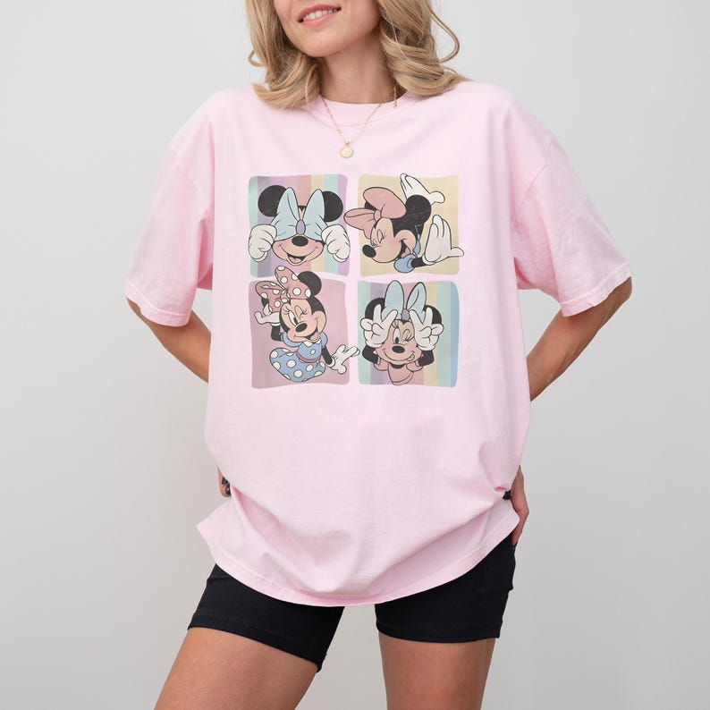 Puede incluir: Camiseta rosa claro con un dise&ntilde;o de cuatro paneles de Minnie Mouse. Cada panel muestra a Minnie en una pose y atuendo diferente, con lazos de varios colores. La camiseta es de corte holgado.