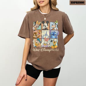 May include: Espresso-coloured t-shirt featuring a grid of Disney characters, including Mickey Mouse, Minnie Mouse, and Stitch. The shirt has the text "Walt Disney World" at the bottom. The shirt is a relaxed fit.