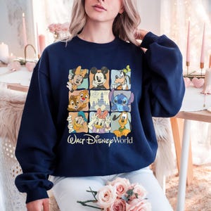 Peut inclure: Sweat-shirt bleu marine avec un motif de grille repr&eacute;sentant des personnages Disney, dont Mickey et Minnie Mouse, Dingo et Stitch. L'inscription "Walt Disney World" est imprim&eacute;e en blanc sous la grille.