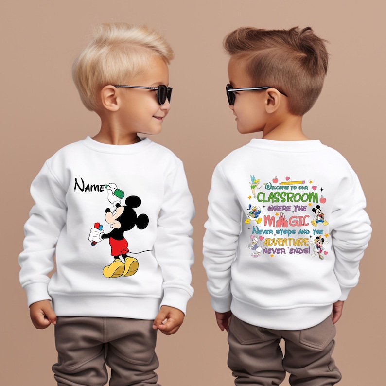 Puede incluir: Sudadera blanca con un dise&ntilde;o de Mickey Mouse sosteniendo un pincel y pintura. La parte delantera de la sudadera tiene la palabra "Name" encima del dise&ntilde;o de Mickey Mouse. La parte trasera de la sudadera tiene el texto "Welcome to our classroom where the magic never stops and the adventure never ends!"