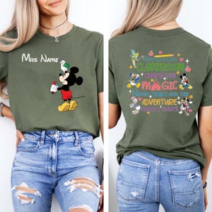 Puede incluir: Camiseta verde oliva con Mickey Mouse sosteniendo un objeto rojo y blanco, y el texto "Mrs Name" arriba. La parte posterior de la camiseta tiene el texto "Welcome to our Classroom Where the Magic Never Stops and the Adventure Never Ends!"