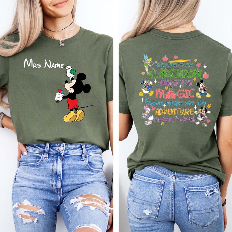 Puede incluir: Camiseta verde oliva con Mickey Mouse sosteniendo un objeto rojo y blanco, y el texto "Mrs Name" arriba. La parte posterior de la camiseta tiene el texto "Welcome to our Classroom Where the Magic Never Stops and the Adventure Never Ends!"