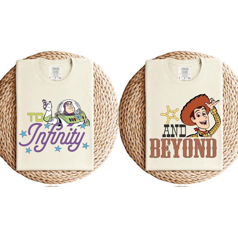 May include: Two cream-coloured t-shirts with cartoon graphics. One features Buzz Lightyear with the text "To Infinity" in purple script. The other shirt displays Woody with the text "And Beyond" in brown letters.
