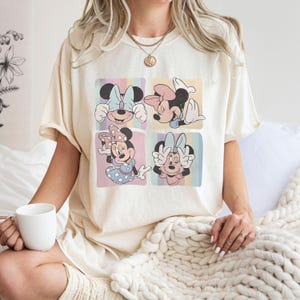 Puede incluir: Camiseta color crema con un dise&ntilde;o de cuatro paneles de Minnie Mouse. Cada panel muestra una pose diferente de Minnie, con fondos pastel y una est&eacute;tica retro. La camiseta es de corte holgado.