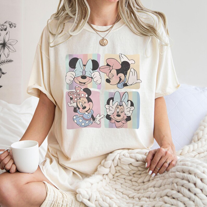 Puede incluir: Camiseta color crema con un dise&ntilde;o de cuatro paneles de Minnie Mouse. Cada panel muestra una pose diferente de Minnie, con fondos pastel y una est&eacute;tica retro. La camiseta es de corte holgado.