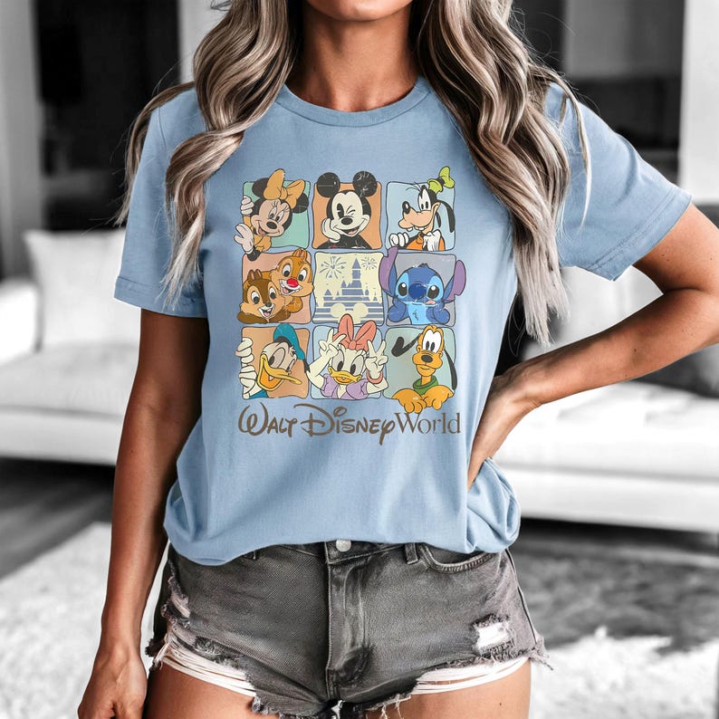 Peut inclure: T-shirt bleu clair avec une grille de personnages Disney, dont Mickey Mouse, Minnie Mouse, Dingo, Donald Duck, Daisy Duck, Tic et Tac, et Stitch. L'inscription "Walt Disney World" est imprim&eacute;e en dessous.