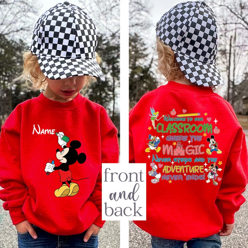 Puede incluir: Una sudadera roja con Mickey Mouse sosteniendo un bol&iacute;grafo, con la palabra "Name" arriba. La parte posterior de la sudadera tiene el texto "Welcome to our classroom where the magic never stops and the adventure never ends" con personajes de Disney.
