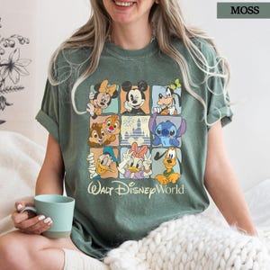 May include: A moss green t-shirt with a grid design showcasing Disney characters such as Mickey and Minnie Mouse, Goofy, Donald and Daisy Duck, Chip and Dale, Stitch, and Pluto. The words "Walt Disney World" are printed below.