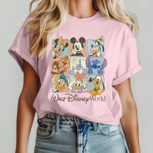 May include: A pale pink t-shirt displaying a grid of nine Disney character portraits, including Mickey Mouse, Minnie Mouse, and Donald Duck. The words "Walt Disney World" are printed in a cursive font below the grid.