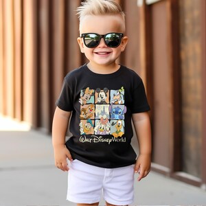Peut inclure: Un t-shirt noir avec une grille de personnages Disney, dont Mickey Mouse et Donald Duck. Le texte "Walt Disney World" est en bas. L'enfant porte un short blanc et des lunettes de soleil noires.