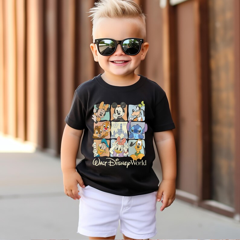 Peut inclure: Un t-shirt noir avec une grille de personnages Disney, dont Mickey Mouse et Donald Duck. Le texte "Walt Disney World" est en bas. L'enfant porte un short blanc et des lunettes de soleil noires.