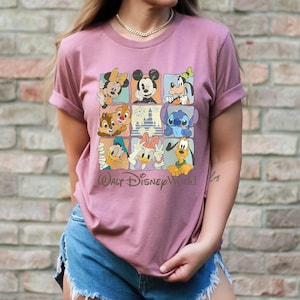 Peut inclure: T-shirt rose poudr&eacute; avec une grille de personnages Disney, dont Mickey Mouse, Minnie Mouse, Dingo, Donald Duck et Daisy Duck. Les mots "Walt Disney World" sont imprim&eacute;s en &eacute;criture cursive sous la grille.