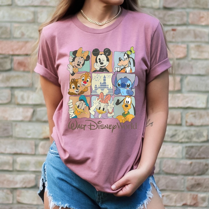 Peut inclure: T-shirt rose poudr&eacute; avec une grille de personnages Disney, dont Mickey Mouse, Minnie Mouse, Dingo, Donald Duck et Daisy Duck. Les mots "Walt Disney World" sont imprim&eacute;s en &eacute;criture cursive sous la grille.