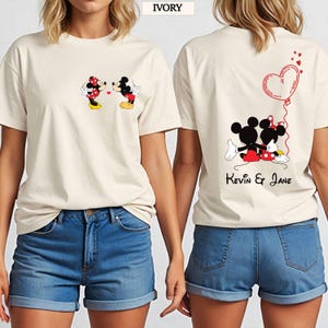 Puede incluir: Camisetas de color marfil con un dise&ntilde;o de Mickey y Minnie Mouse. La parte delantera de la camiseta muestra a los personajes bes&aacute;ndose. La parte trasera de la camiseta tiene un globo en forma de coraz&oacute;n y el texto "Kevin & Jane".