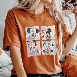 Puede incluir: Camiseta naranja quemado con un dise&ntilde;o de cuatro paneles de Minnie Mouse en varias poses. Cada panel tiene un fondo de arco&iacute;ris pastel. Minnie lleva lazos y vestidos en los paneles. La camiseta es de estilo c&oacute;modo e informal.