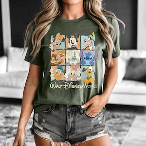 Peut inclure: T-shirt vert olive avec une grille de personnages Disney, dont Mickey Mouse, Minnie Mouse et Donald Duck. L'inscription "Walt Disney World" est imprim&eacute;e en dessous de la grille.