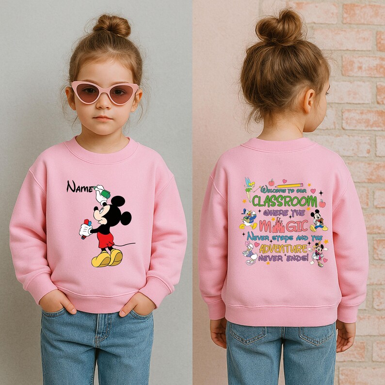 Puede incluir: Sudadera rosa con un dibujo de Mickey Mouse sosteniendo un helado rojo y un objeto verde y blanco. La palabra "Name" est&aacute; encima del dibujo de Mickey Mouse. La parte trasera de la sudadera tiene el texto "Welcome to our classroom where the magic never stops and the adventure never ends!"
