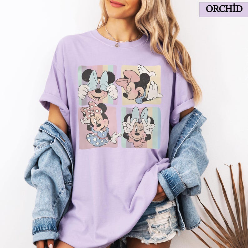 Puede incluir: Camiseta morada orqu&iacute;dea con un gr&aacute;fico de Minnie Mouse en cuatro poses diferentes, cada una en un cuadrado de color pastel. La camiseta tiene mangas cortas y un corte holgado. La palabra "ORCHID" est&aacute; impresa en un recuadro en la esquina superior derecha.