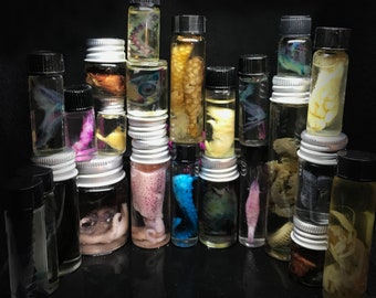 May include: A collection of small glass bottles filled with preserved specimens. The bottles are arranged in a stacked formation against a dark background. The specimens include various marine life and biological samples, showcasing a variety of colors and textures.