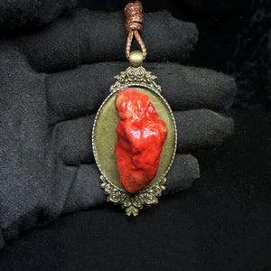 Peut inclure: Un pendentif en forme de cœur rouge dans un cadre orné doré, suspendu à un cordon brun. Le pendentif est une pièce de bijouterie unique et accrocheuse.