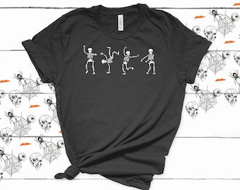 May include: A black t-shirt featuring a graphic of four skeletons dancing. The skeletons are white and are in different poses. The shirt is made from a soft, comfortable material.