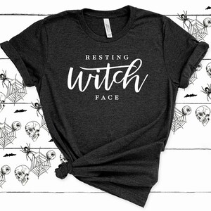 May include: A dark gray t-shirt with the text "Resting Witch Face" in white lettering.