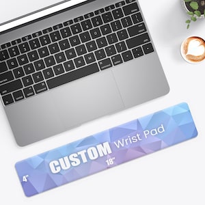 K&ouml;nnte beinhalten: Ein Handgelenkst&uuml;tze mit geometrischem Muster in Blau und Lila mit dem Text "CUSTOM Wrist Pad" und den Ma&szlig;en "4" und "18" Zoll.