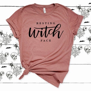 May include: A mauve t-shirt with the text "Resting Witch Face" printed in black.