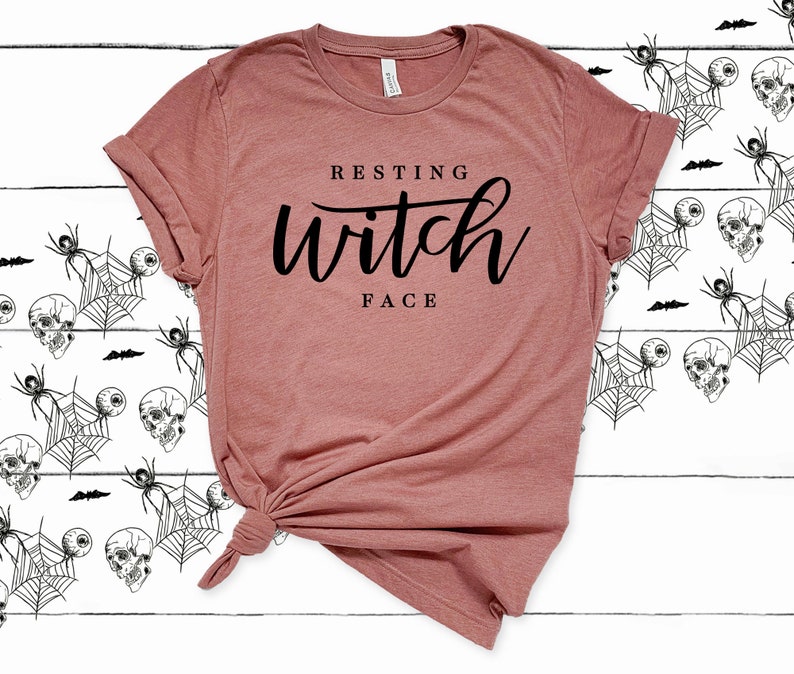 May include: A mauve t-shirt with the text "Resting Witch Face" printed in black.
