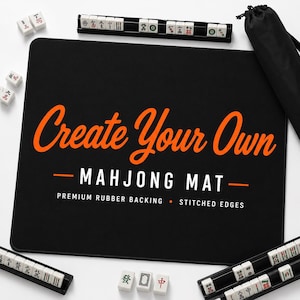 May include: A black rectangular mahjong mat with orange and white text reading Create Your Own MAHJONG MAT, PREMIUM RUBBER BACKING, STITCHED EDGES. The mat is surrounded by several white mahjong tiles, black tile racks, and a black drawstring bag.