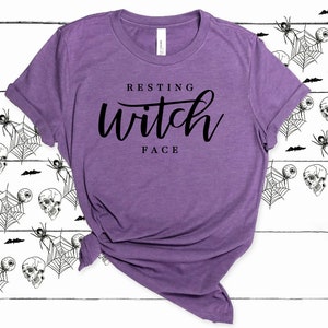 May include: Purple t-shirt with the text "Resting Witch Face" in black lettering.