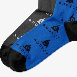 May include: Two pairs of socks, one charcoal gray and one bright blue, are displayed. The blue sock has a black heel and toe, and features a repeating pattern of a geometric design and the word "ADDYCT" in black. The gray sock has a white logo and the word "ADDYCT".