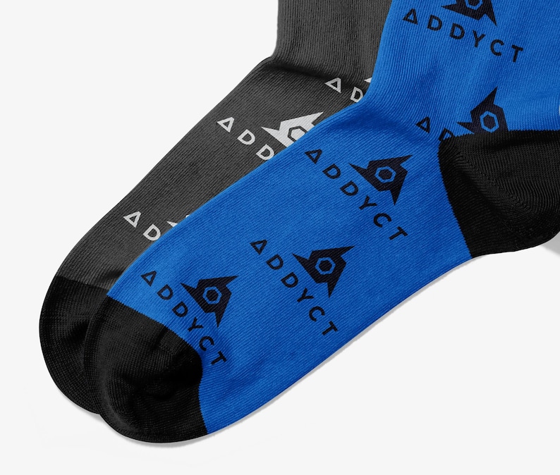 May include: Two pairs of socks, one charcoal gray and one bright blue, are displayed. The blue sock has a black heel and toe, and features a repeating pattern of a geometric design and the word "ADDYCT" in black. The gray sock has a white logo and the word "ADDYCT".
