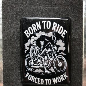 May include: Black rectangular magnet with the text "BORN TO RIDE FORCED TO WORK" and a skeleton riding a motorcycle. The skeleton is holding a mug. The design is in white and silver against a black background.