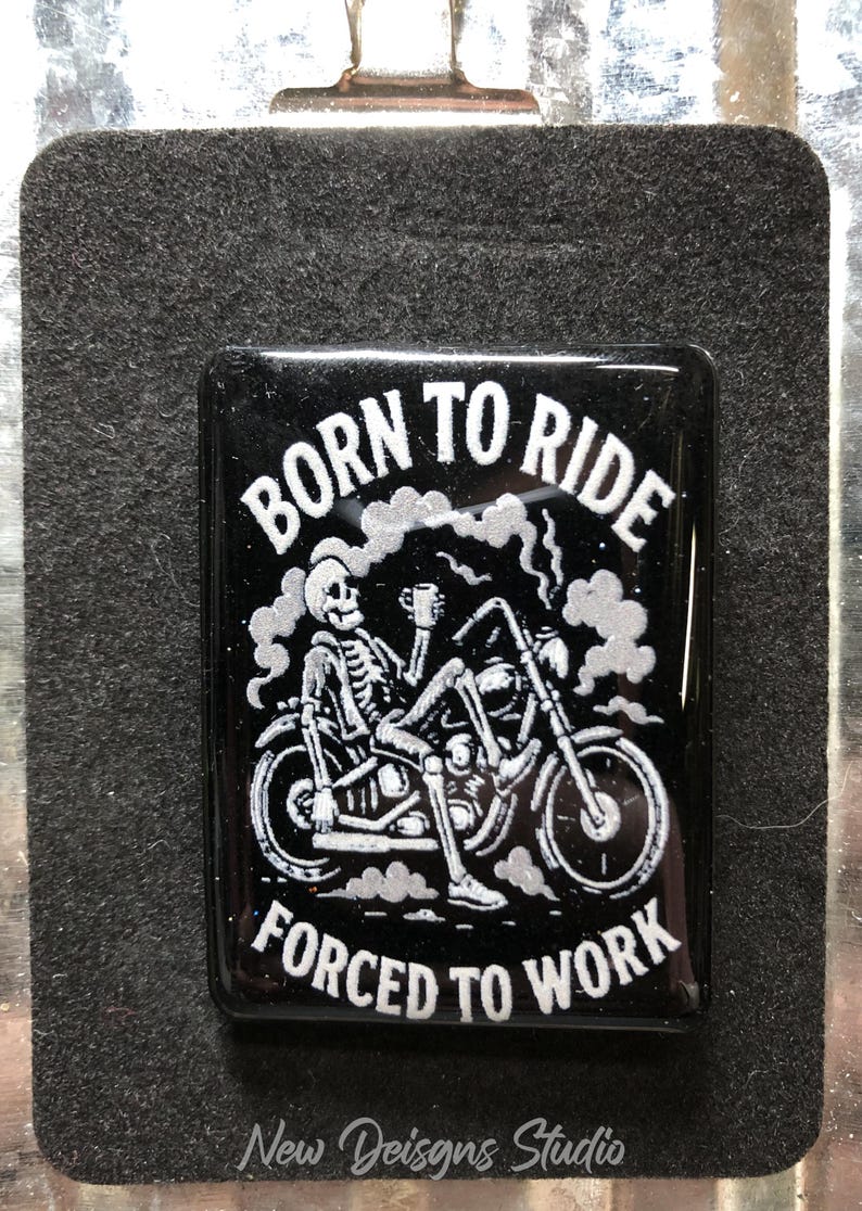 May include: Black rectangular magnet with the text "BORN TO RIDE FORCED TO WORK" and a skeleton riding a motorcycle. The skeleton is holding a mug. The design is in white and silver against a black background.