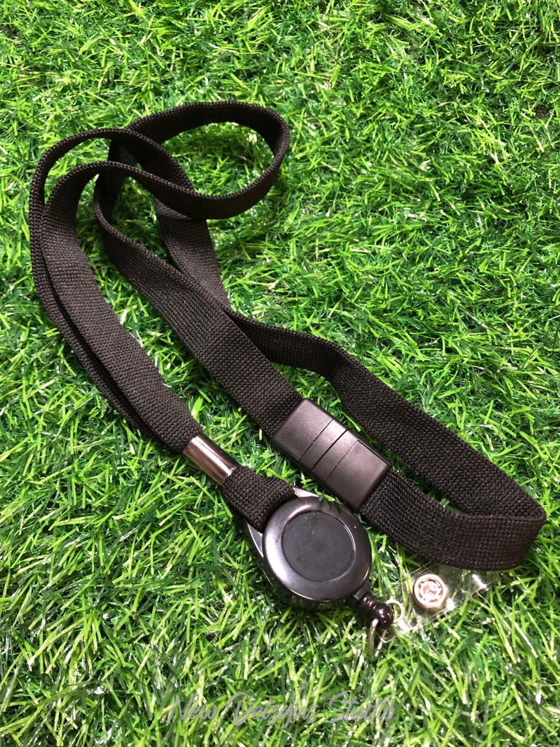 May include: Black lanyard with a retractable badge reel and a clear plastic badge holder. The lanyard is made of a woven fabric and has a black plastic clasp. The badge reel is round and black, with a metal clip.
