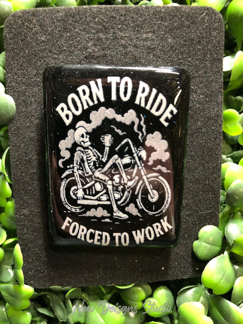 May include: A black rectangular resin piece with the words "BORN TO RIDE" and "FORCED TO WORK" in white. A skeleton is riding a motorcycle, holding a mug. The background is black with a glittery effect.