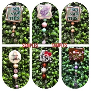 May include: A collection of decorative badge reels with various designs and text. The reels feature phrases like "Not Enough Sage For This", "Best Mom", "Stronger Together", and "ER Nurse". Each reel has a unique bead and charm arrangement.