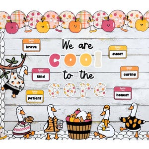 May include: A classroom display with a white wooden backdrop. The phrase "We are cool to the core" is written with apple-themed letters. Apple cutouts and labels with positive words such as "brave" and "kind" are visible. Illustrations of geese are also present.
